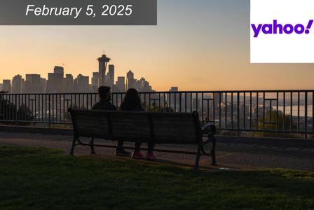 Two people sit on a bench overlooking a city skyline at sunset. The date 