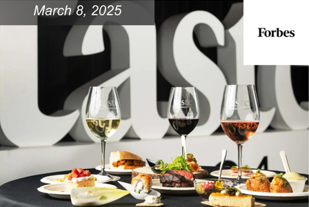 A selection of gourmet dishes and wine glasses on a black tablecloth, with plates of assorted appetizers and entrees. The background shows the word 