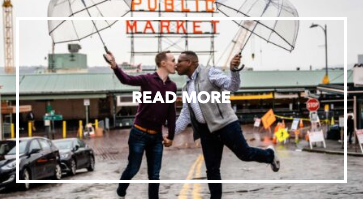 Image of two men holding umbrellas and kissing in front of an iconic red sign in Pike Place Market.