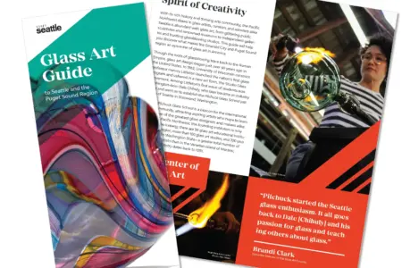 Two colorful brochures about Seattle's glass art scene are displayed. The covers feature vibrant glasswork and artists in action. Text highlights the spirit of creativity and mentions local artists and a quote from Brandt Clark.