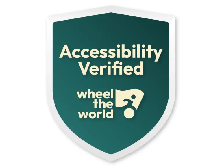 A green shield with white trim displays the text "Accessibility Verified" above the logo "wheel the world," which features a stylized wheelchair symbol.